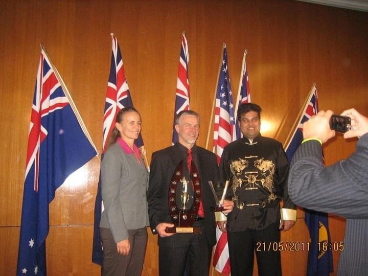 Ryan Gomez receiving an award at an international speaking competition with Australian and American flags