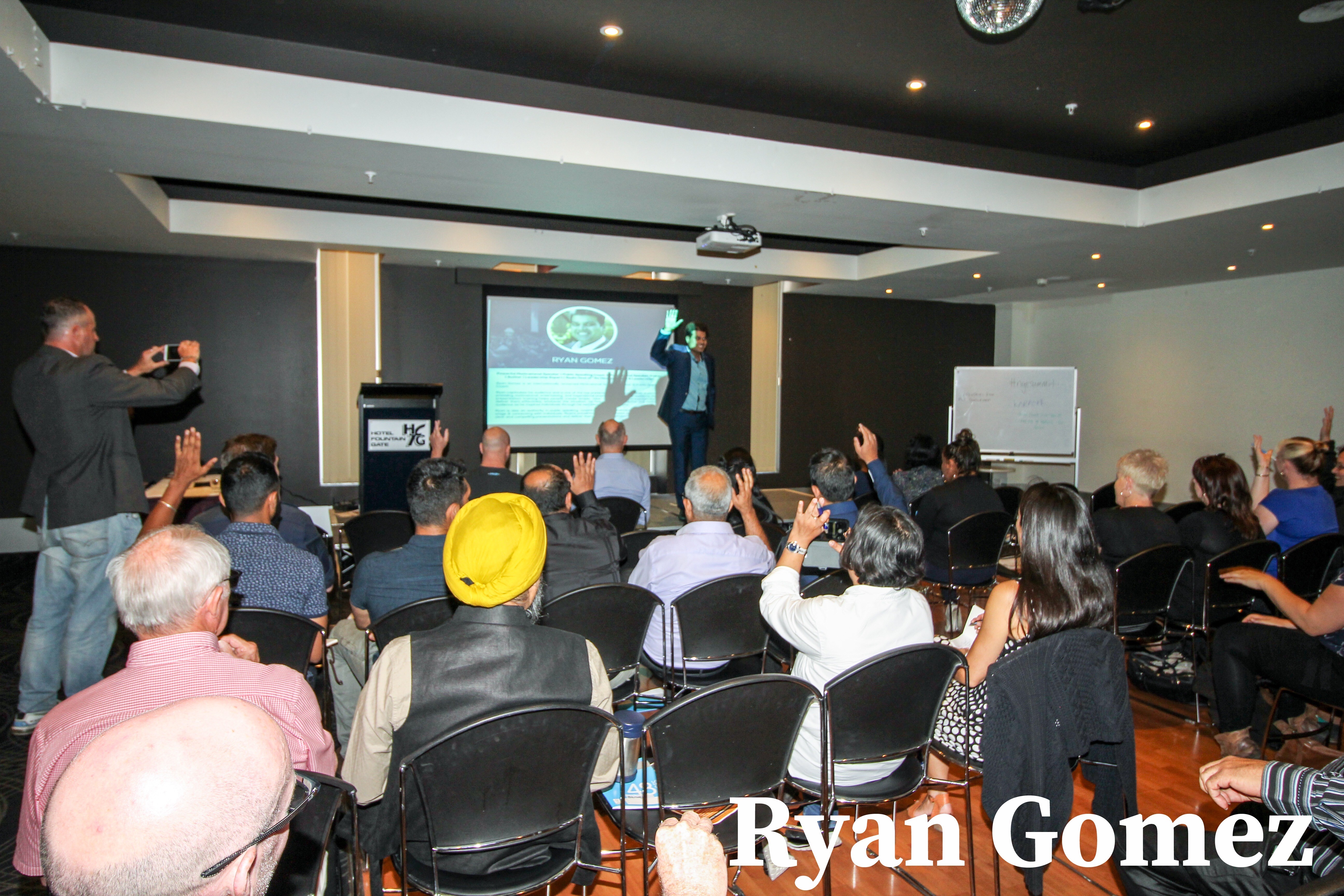 Ryan Gomez presenting to a packed room at Hotel Fountain Gate — audience engaged with hands raised